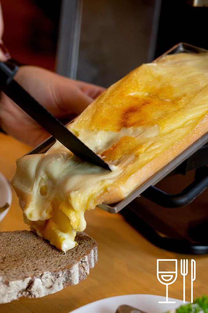 eine Person schabt heißen Käse auf ein Brot