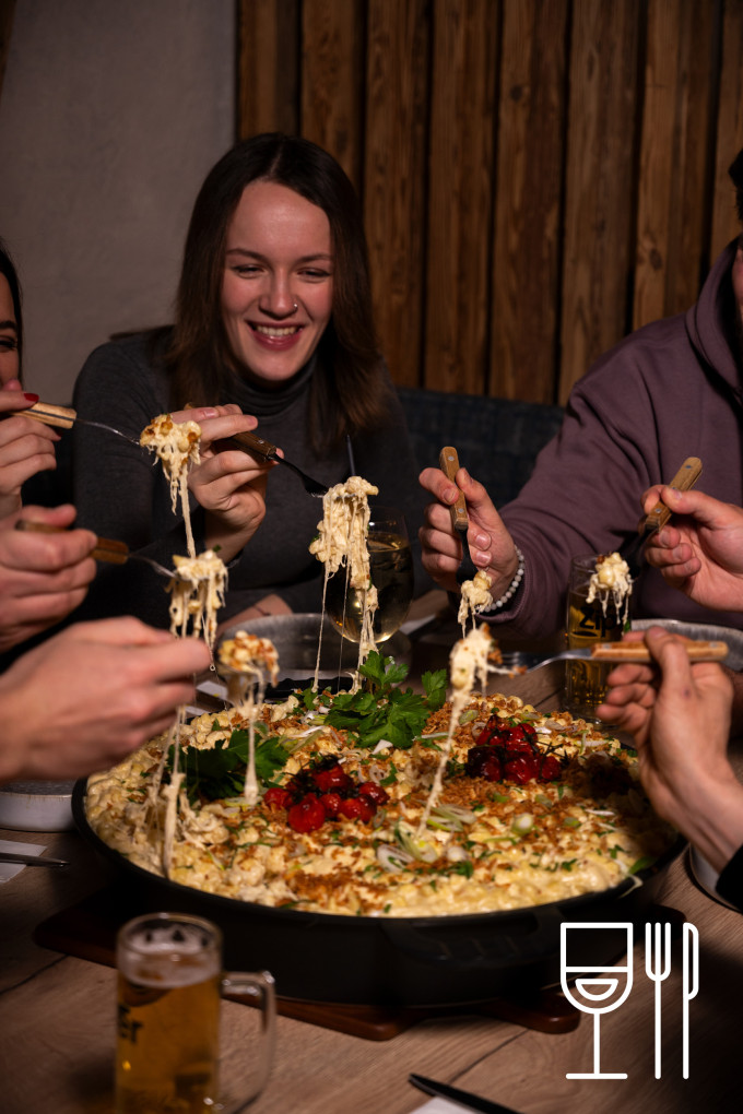 Eine Gruppe von Menschen, die Käsespätzle aus einer Riesenpfanne essen