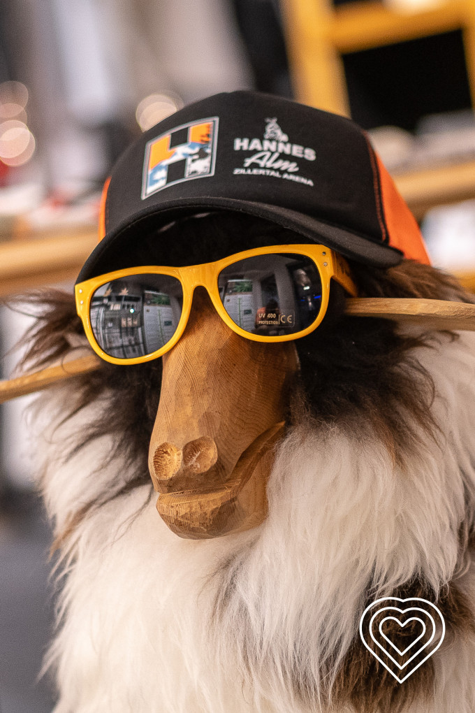 ein hölzernes Schaf welches eine Hannes Alm Cap und Sonnenbrille trägt
