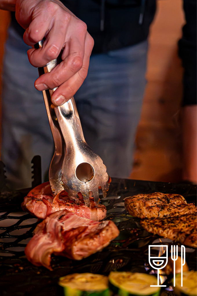 eine Hand die mit einer Zange das Fleisch am Grill hält