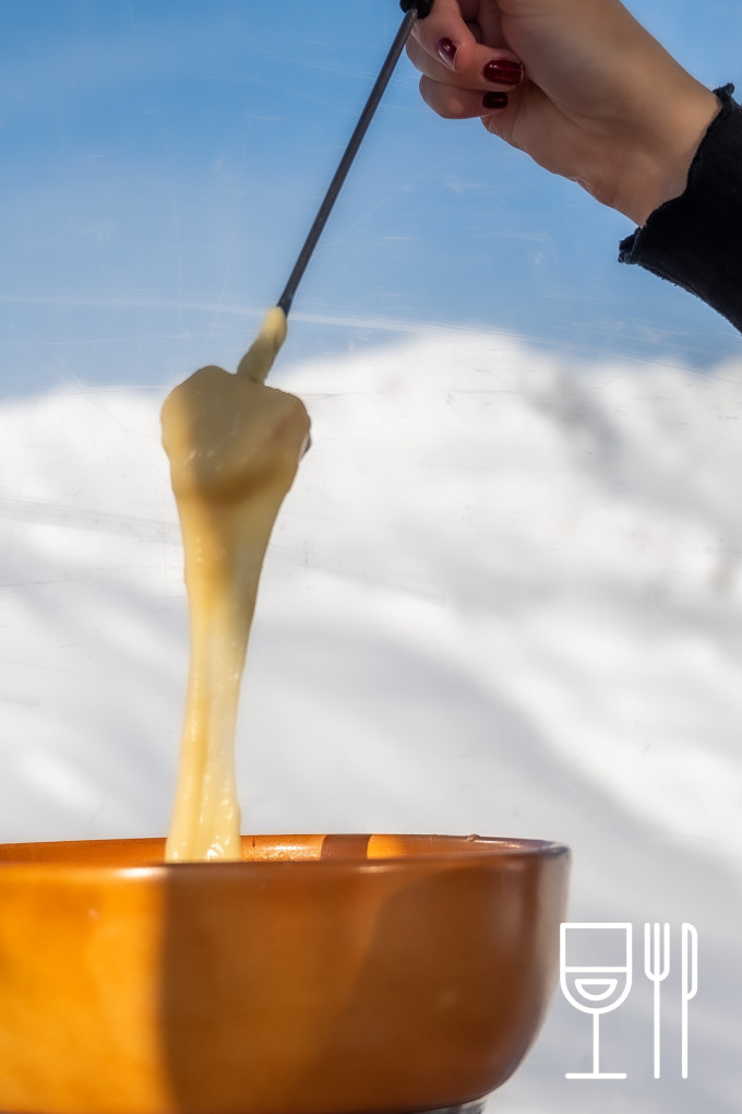eine Hand die im Fondue den Käse hochzieht